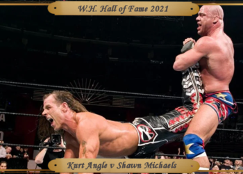 Angle holds Michaels in the ankle lock. Michaels is parallel to the mat, perched up on his elbows in pain.