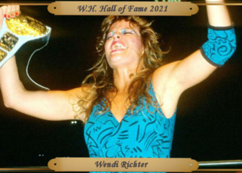 Richter, wearing a teal women's singlet and a teal elbow pad on her left arm, holding both arms up, with the WWF Women's World Championship belt in her right hand after a successful match.