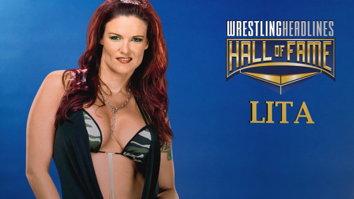Lita has dark red dyed hair that falls past her shoulders on top the tops of her breasts. She is wearing a dark green and grey camouflaged bra, and a thin, black vest draped over that.