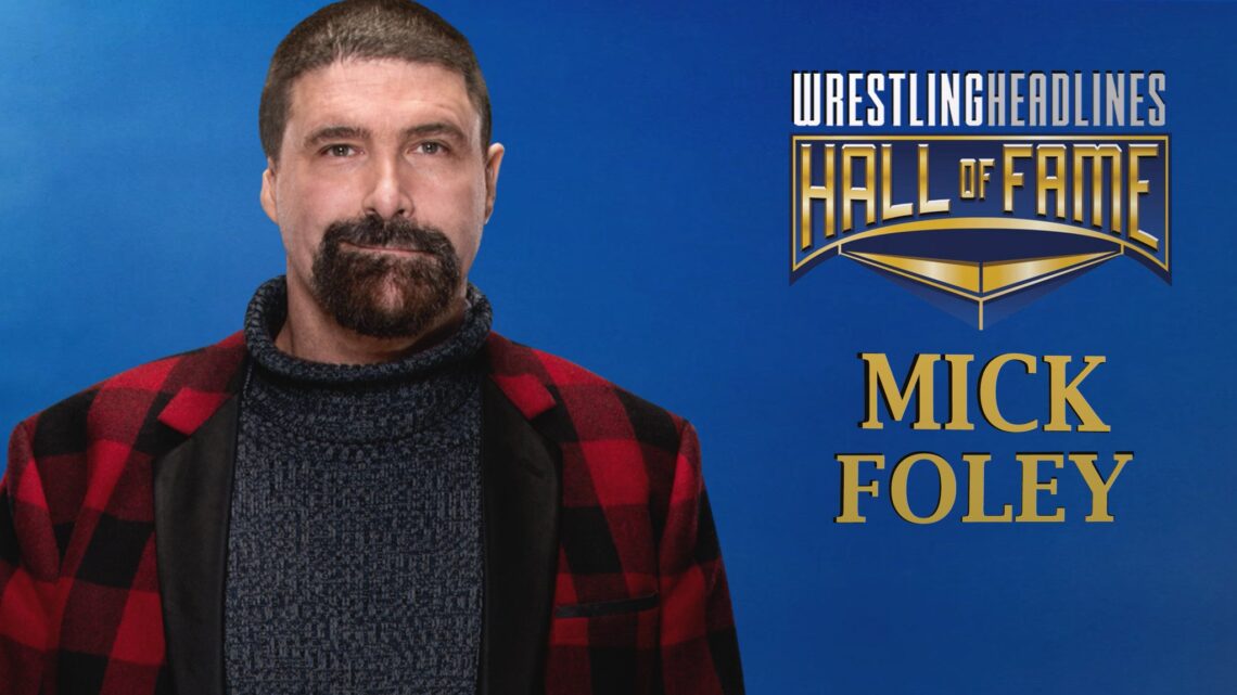 Mick Foley, in more recent days, wearing a red and black flannel suit jacket and a grey turtleneck.