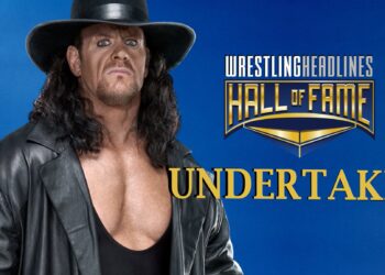 Undertaker stands with his trademark, wide-brimmed, black hat, shoulder length hair, open black leather jacket and black tank-top revealing most of his chest.