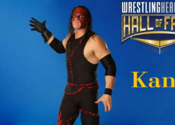 Kane, wearing his more recent red and black demon mask that does not cover his mouth, is standing with his right, black-gloved hand stretched out ready to chokeslam his opponent. He is wearing his mostly black spandex one-piece suit with the red stitching on it.